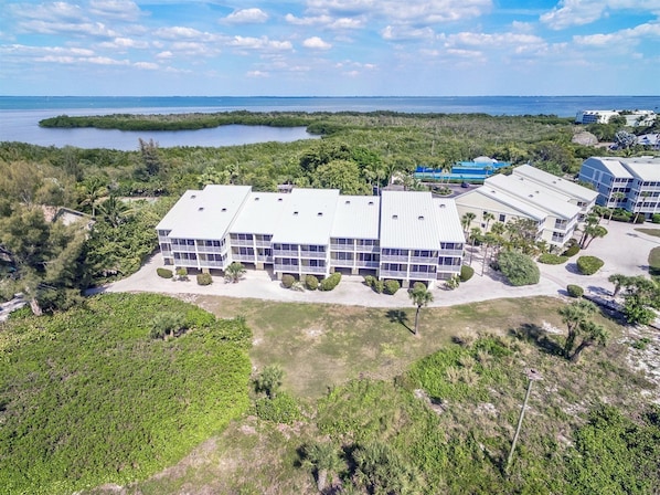 A multi-story building with a flat roof, surrounded by greenery and a body of water.