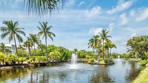 A tranquil water feature with fountains, surrounded by lush greenery and palm trees, with buildings in the background. - Beach Villas (Captiva)