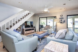 A modern living room with a staircase, a flat-screen TV, and a dining area with a table and chairs.