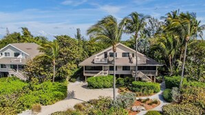 A two-story beachfront house with a balcony, surrounded by lush greenery and palm trees. - South Seas Gulf Cottage 1106 (Captiva)