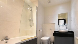 A modern bathroom with a glass-enclosed shower, a white toilet, and a black sink with a glass shelf. - The Carlton Manor Hotel (Lowestoft)