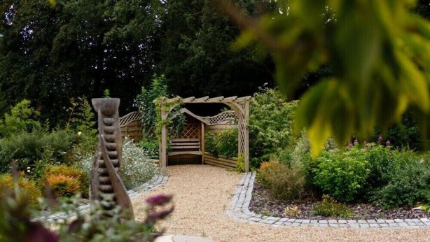 A garden pathway leading to a wooden pergola with a lattice design, surrounded by various plants and shrubs. - The Carlton Manor Hotel (Lowestoft)