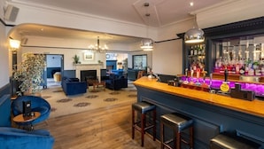 A bar area with a wooden counter, stools, and a bar stocked with bottles. - The Carlton Manor Hotel (Lowestoft)