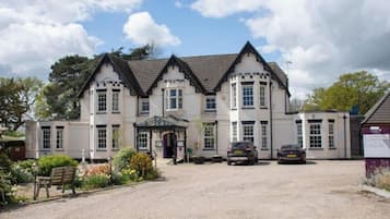A two-story building with a symmetrical facade, a gravel driveway, and parked cars.