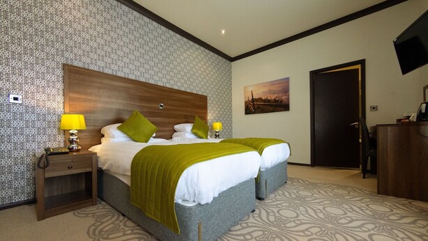 A hotel room with a large bed, two bedside tables with lamps, a desk, and a chair. - The Carlton Manor Hotel (Lowestoft)