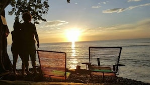 Dos sillas de metal mirando al atardecer sobre una masa de agua.
