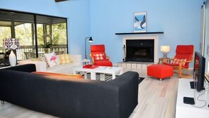 Una sala de estar moderna con un sofá negro, sillones rojos, una mesa de centro blanca y una chimenea.