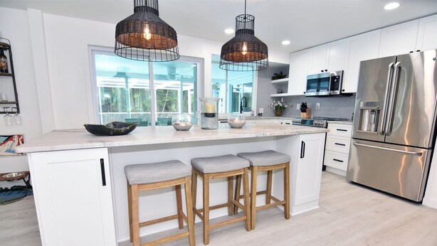 Een moderne keuken met witte kasten, roestvrijstalen apparatuur en een groot kookeiland met barkrukken.