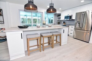 A modern kitchen with white cabinetry, stainless steel appliances, and a large island with bar stools. - Palm Home (Sanibel)