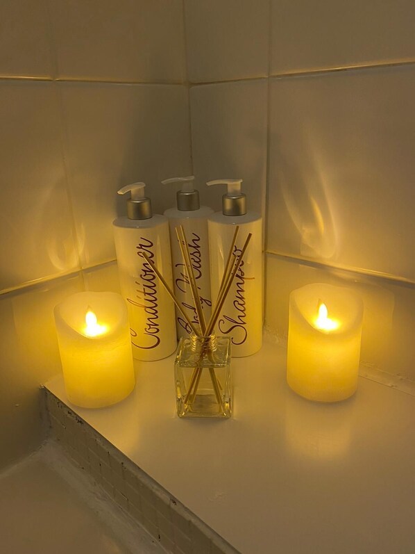 A bathroom with three bottles of Connaissance de L'Essence de Shampoo and two lit candles. - Cosy Riverside Apartment - Woodsmill Quay Free Parking (York)