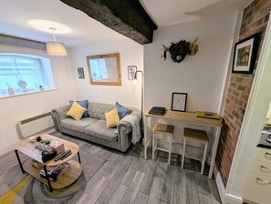 A cozy room with a grey sofa, a wooden table, a small desk, and a brick wall.