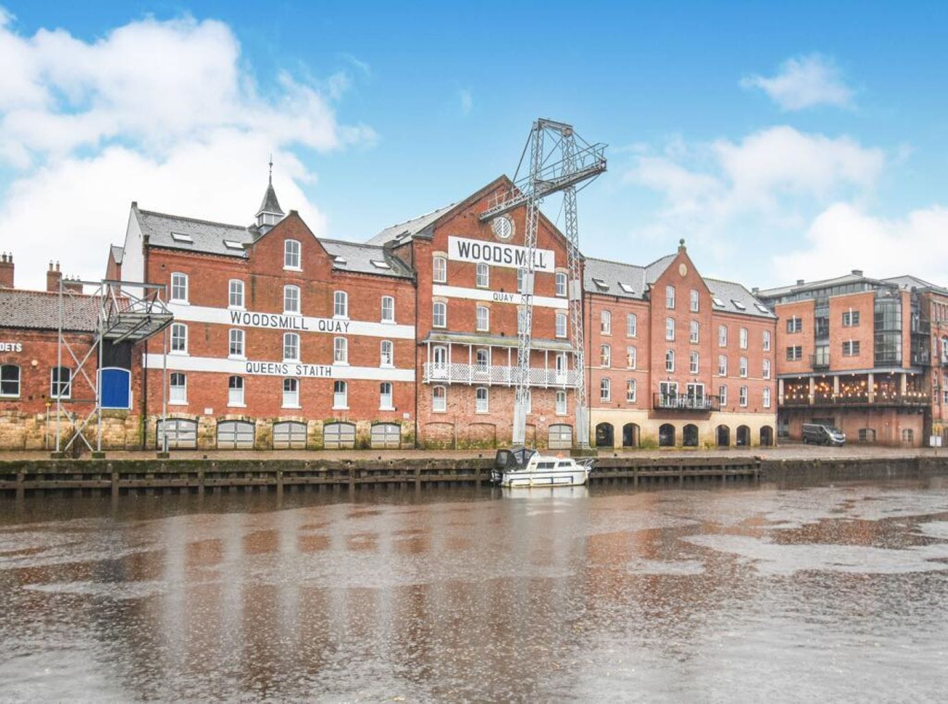 A waterfront building with multiple levels and a crane, adjacent to a river.