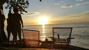 Deux chaises en métal, placées face à face, offrent une vue sur un coucher de soleil se reflétant sur une étendue d’eau.