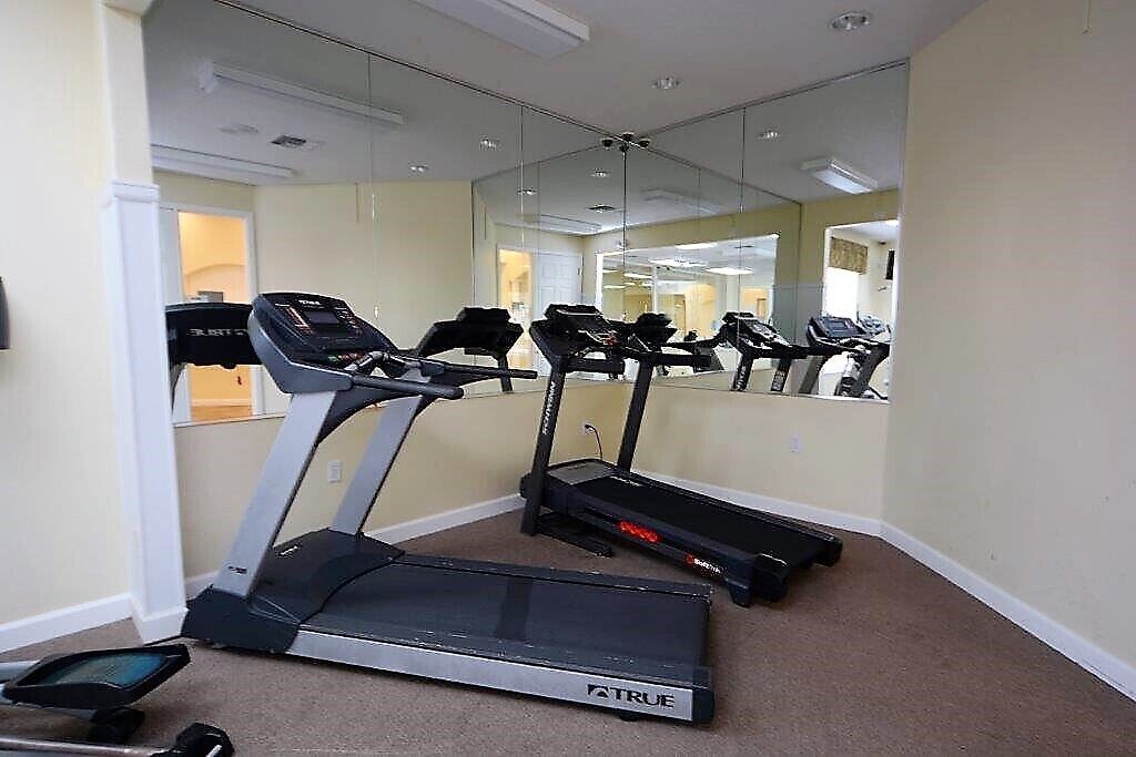 Un gimnasio con cintas de correr, un espejo grande y suelo alfombrado.