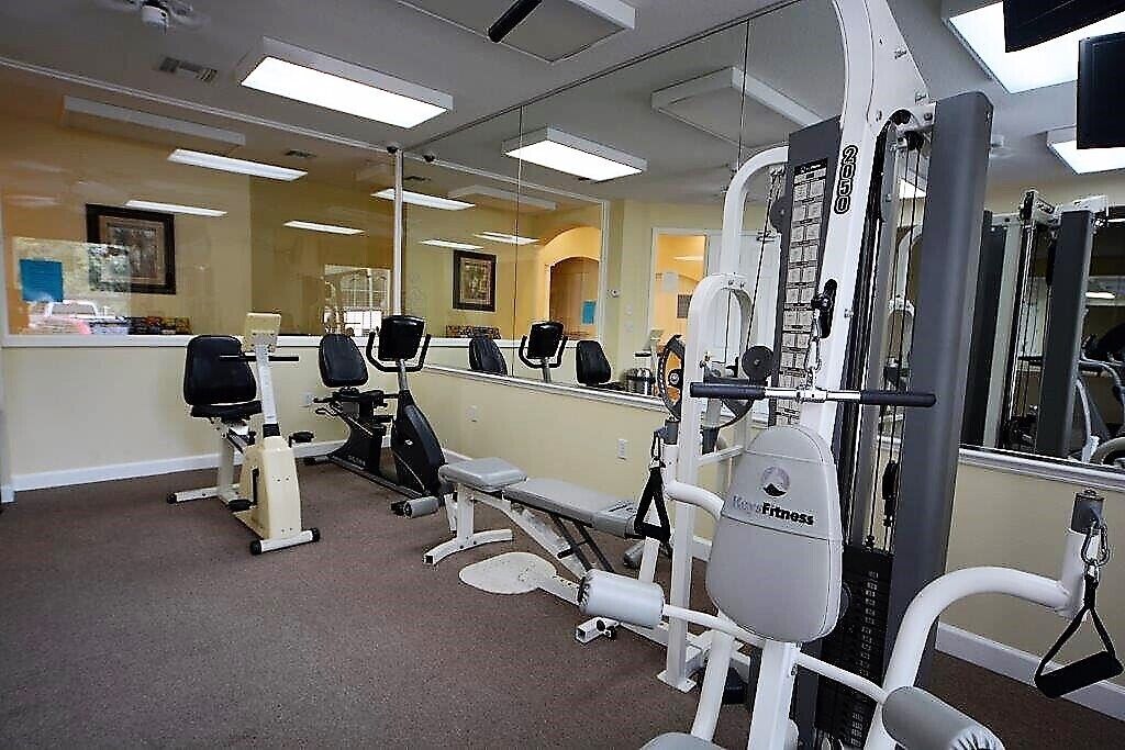 Un gimnasio con equipo de ejercicio, un mostrador de recepción y un espejo grande.