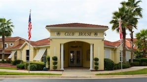 A Club House with a yellow facade, red-tiled roof, and a central entrance flanked by palm trees and American flags. - Private Pool Home-popular Resort Near Disney! (Kissimmee)