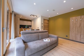 Un salon moderne avec un canapé gris, un plancher en bois et une cuisine en arrière-plan.