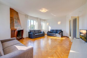 Ein geräumiges Wohnzimmer mit Kamin, zwei Sofas, einem Fernseher und großen Fenstern.
