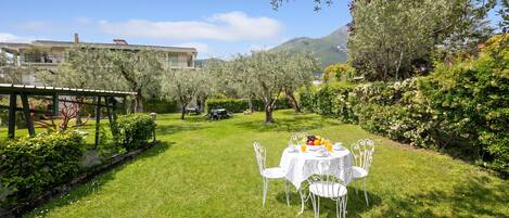 A well-maintained garden with a table set for a meal, surrounded by greenery and a mountain in the background.