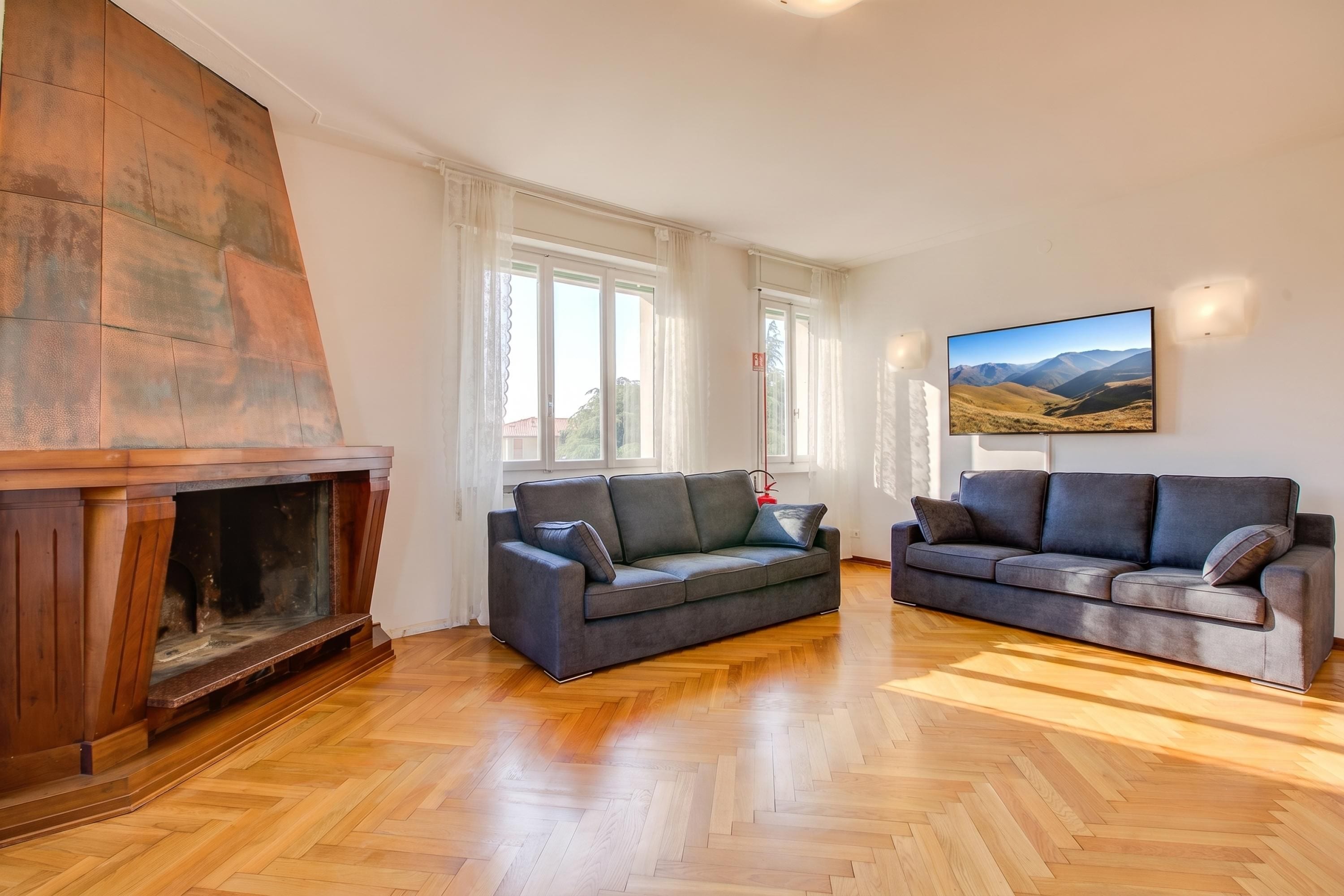 A living room with a fireplace, two sofas, a large window, and a painting on the wall.