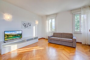 A modern living room with a flat-screen TV, a grey sofa, and a white entertainment unit. - Margherita Near Lake - Family Friendly (Toscolano Maderno)