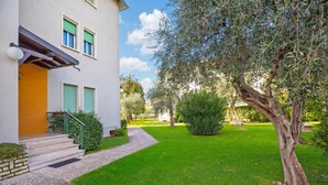 A two-story building with a yellow facade, green shutters, and a well-maintained lawn. - Margherita Near Lake - Family Friendly (Toscolano Maderno)