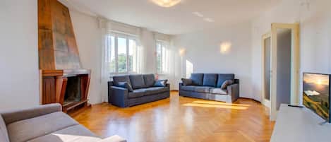Un salon spacieux avec une cheminée, deux canapés, un téléviseur et de grandes fenêtres.