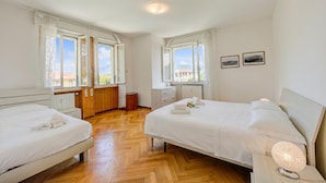 A hotel room with two beds, a wooden floor, a window with curtains, a bedside table with a lamp, and a radiator. - Margherita Near Lake - Family Friendly (Toscolano Maderno)
