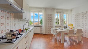A kitchen with a stove, sink, and dining area with chairs and a table. - Margherita Near Lake - Family Friendly (Toscolano Maderno)