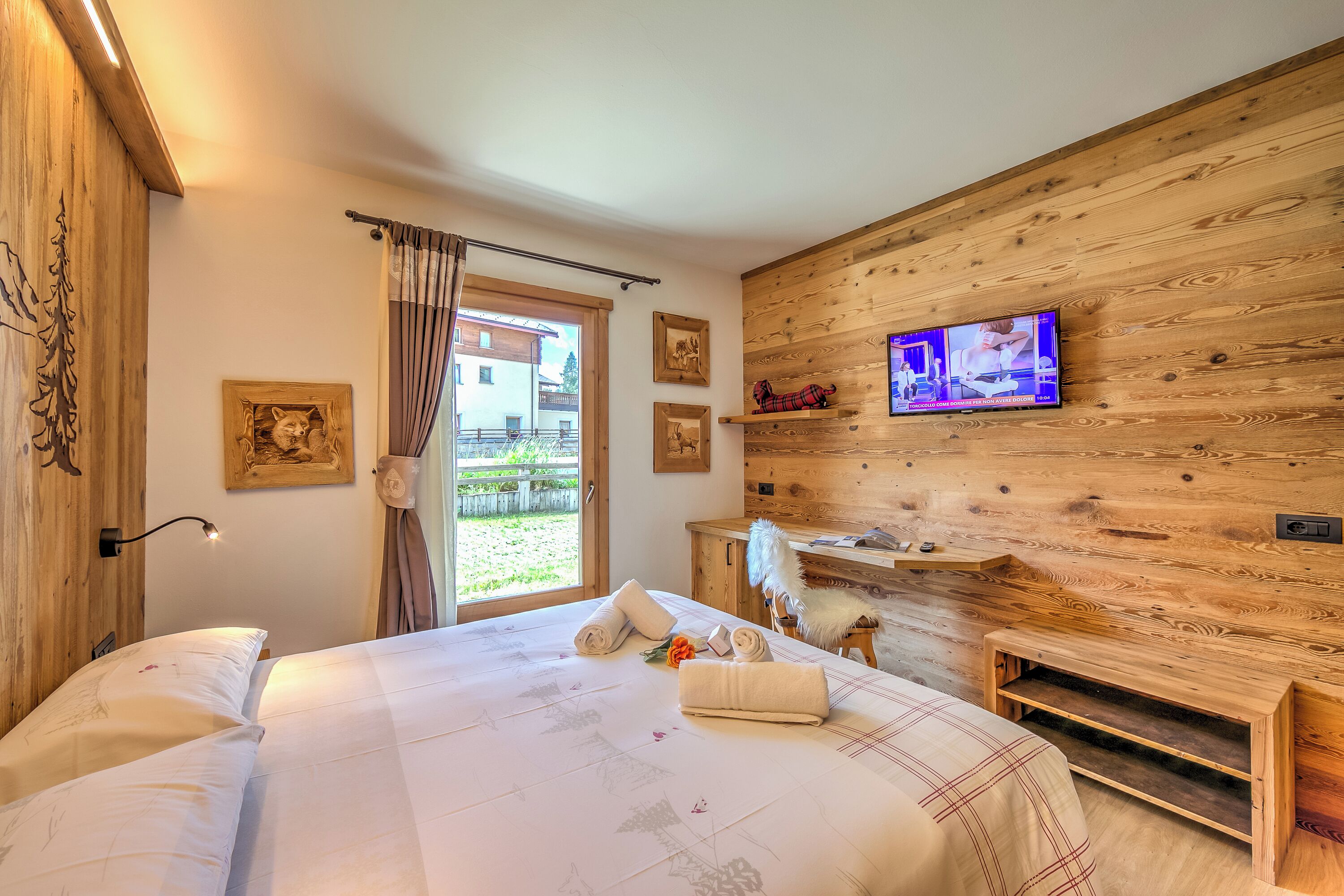 A bedroom with a wooden wall, a TV, and a bed with towels.