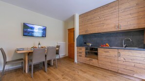 Eine moderne Küche mit Holzschränken, einem Esstisch mit Stühlen und einem an der Wand befestigten Fernseher.