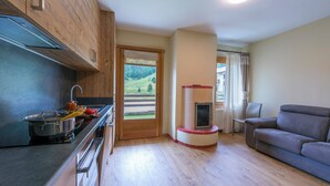 Eine moderne Küche mit Herd, Spüle und Holzausbau. Ein Essbereich mit Tisch und Stühlen sowie ein Wohnzimmer mit Sofa. Ein Fenster bietet Blick auf eine grüne Landschaft.
