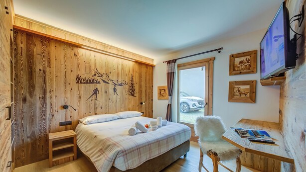 Ein Schlafzimmer mit einem Bett, einem Sessel, einem kleinen Tisch, einem Fernseher und einem Fenster, vor dem ein Auto parkt.