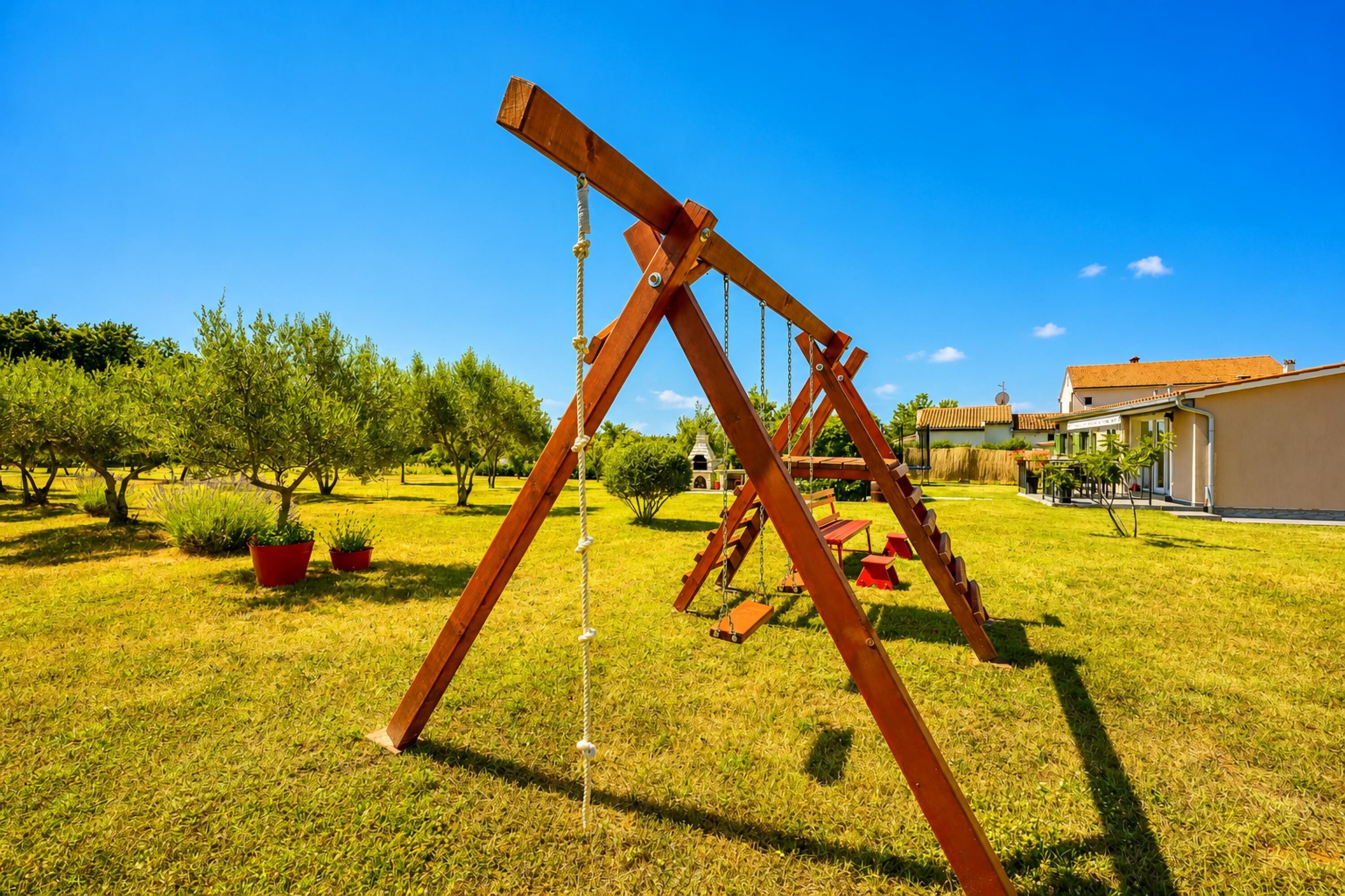 Un ensemble de balançoires en bois installé dans une cour verdoyante, avec une maison en arrière-plan.