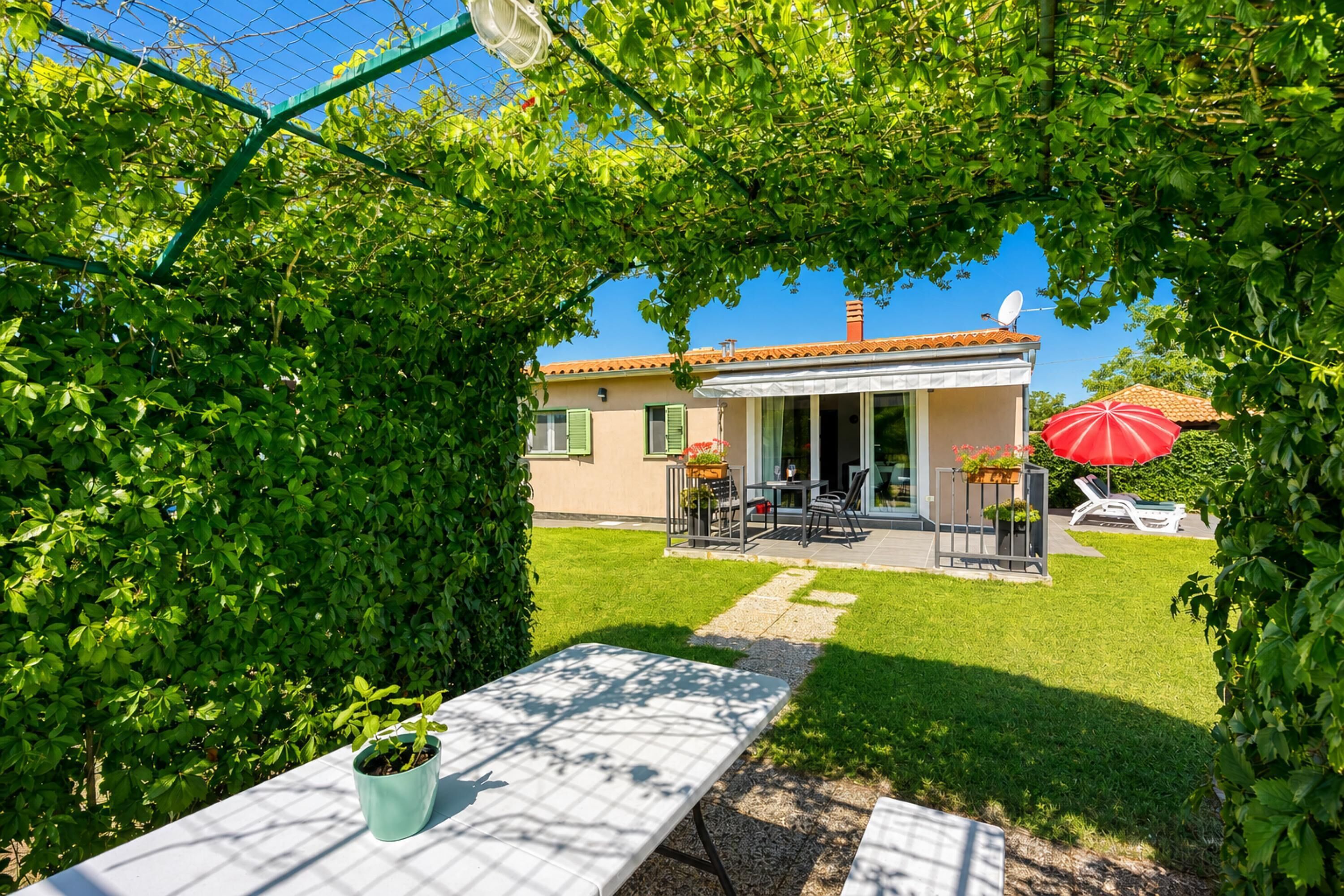A house with a patio, a table with a potted plant, and a red umbrella.