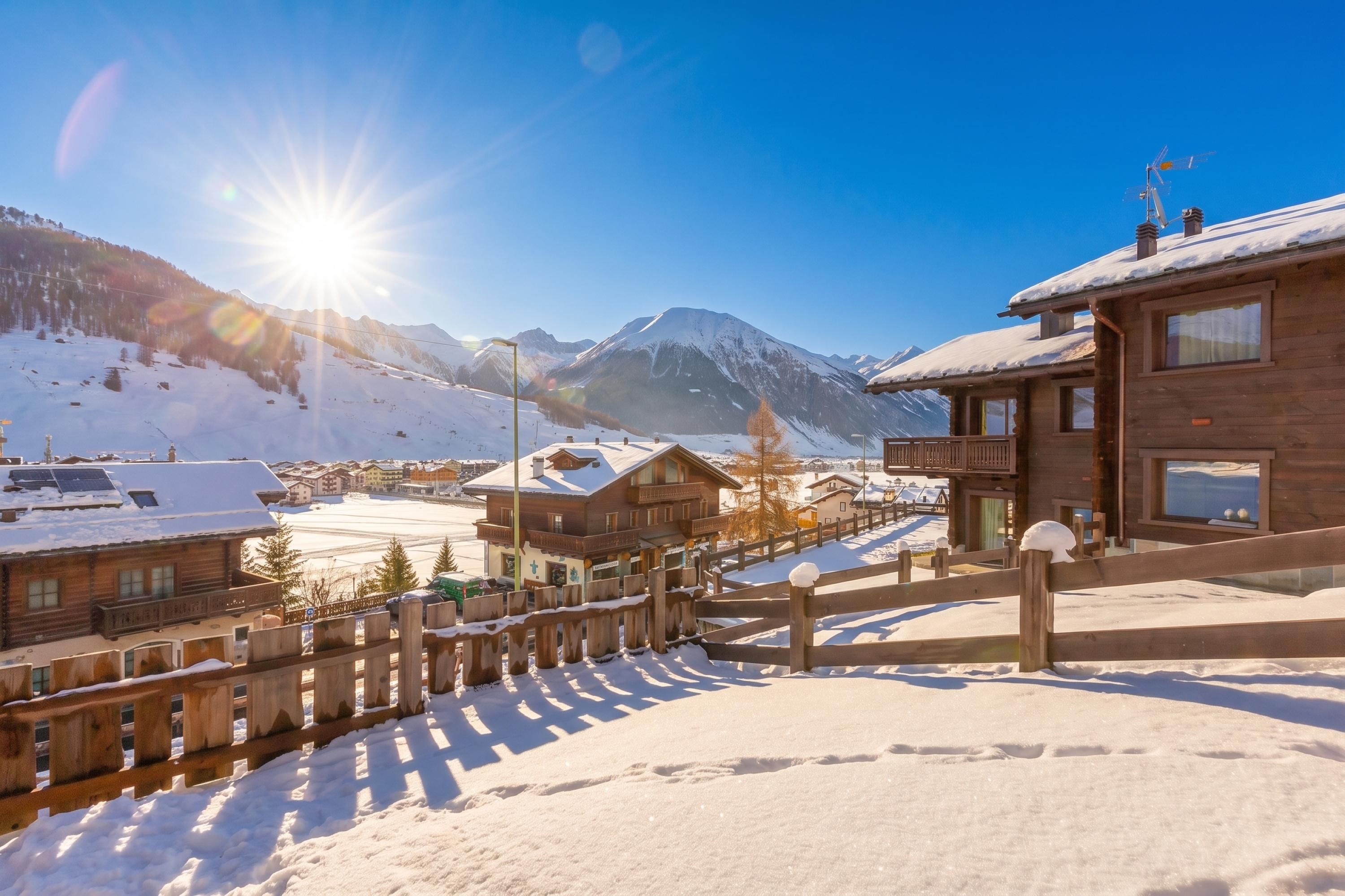 Eine Holzchalet mit Balkon, umgeben von verschneitem Gelände und Bergen im Hintergrund.