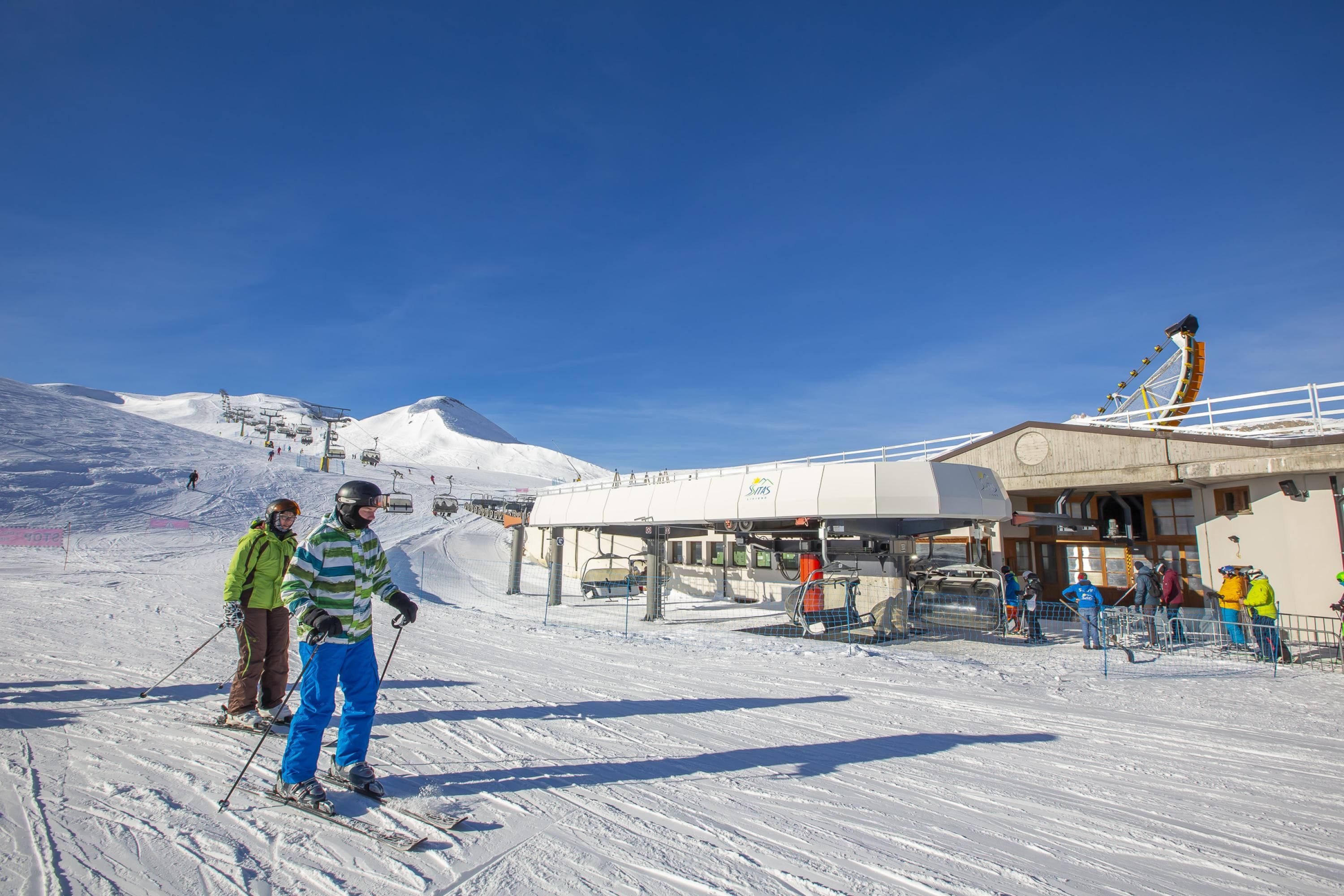 Une station de ski avec un télésiège, un bâtiment portant une enseigne et une pente enneigée.
