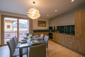 Una cocina moderna con armarios de madera, una mesa de comedor preparada para cuatro personas y un ventanal con vistas a un balcón.