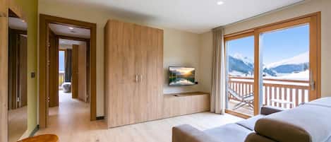 Ein Hotelzimmer mit großem Fenster, einer Couch, einem Fernseher und einem Holzschrank.