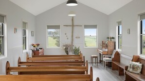 Ein Kircheninneres mit Holzbänken, einem Klavier und einem Kruzifix an der Wand.