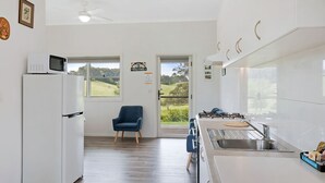 Eine moderne Küche mit Einbauherd, Mikrowelle und Kühlschrank. Ein blauer Stuhl und eine Tür zu einem Balkon mit Blick auf eine grüne Landschaft.