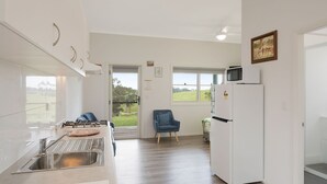 Een moderne keuken met een roestvrijstalen spoelbak, een magnetron en een koelkast. Er staat een blauwe stoel en er is een raam met uitzicht op de omgeving.