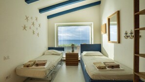 A room with two beds, a window with a view of the sea, starfish wall decor, and a wooden cabinet. - Domus of the Sea: villa with cliffside pool in the heart of Gallura (Trinità d'Agultu e Vignola)