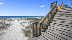 Un escalier en bois mène à des chaises de plage qui offrent une vue sur une plage de sable et l’océan.