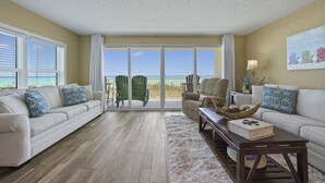 Una sala de estar con un sofá color beige, una mesa de centro y vista a la playa a través de amplios ventanales.