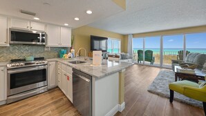 Una cocina moderna con una isla central, un comedor con vistas y una sala de estar con una silla verde y un reposapiés amarillo.