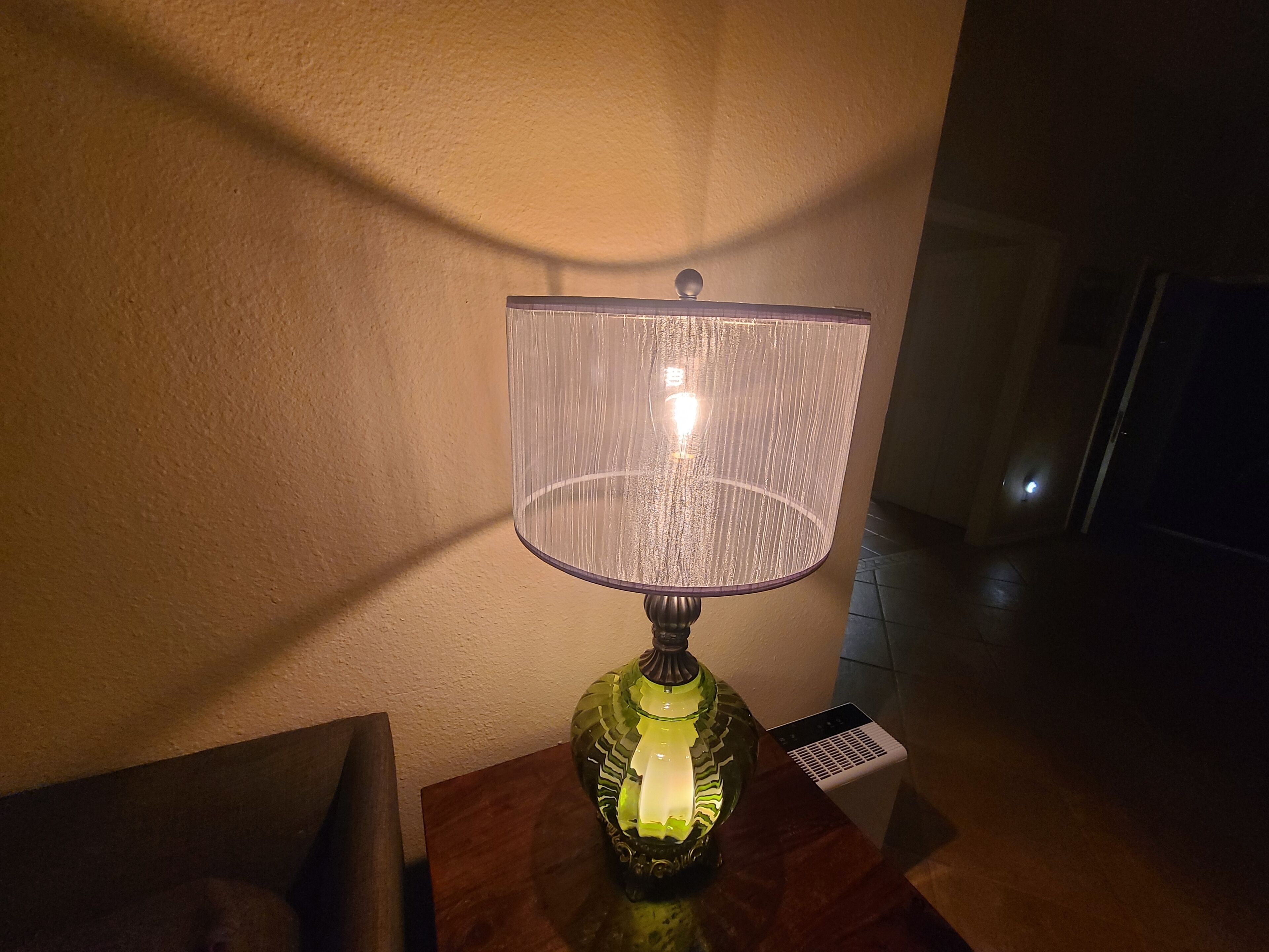 Una lampada da tavolo con paralume trasparente su un tavolo di legno in una stanza poco illuminata.