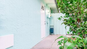 A narrow, light blue-painted corridor with a concrete floor, a white door, and a blue chair.
