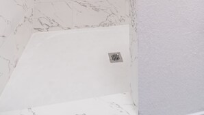 A shower with white marble tiles and a silver showerhead.