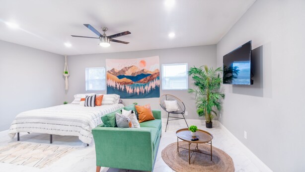 A modern bedroom with a bed, a green armchair, a round coffee table, and a ceiling fan.